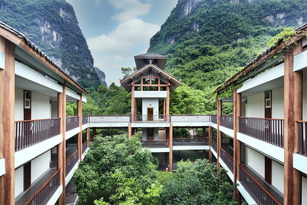 Timber-framed courtyard wings of Yangshuo Resort beneath forested karst peaks