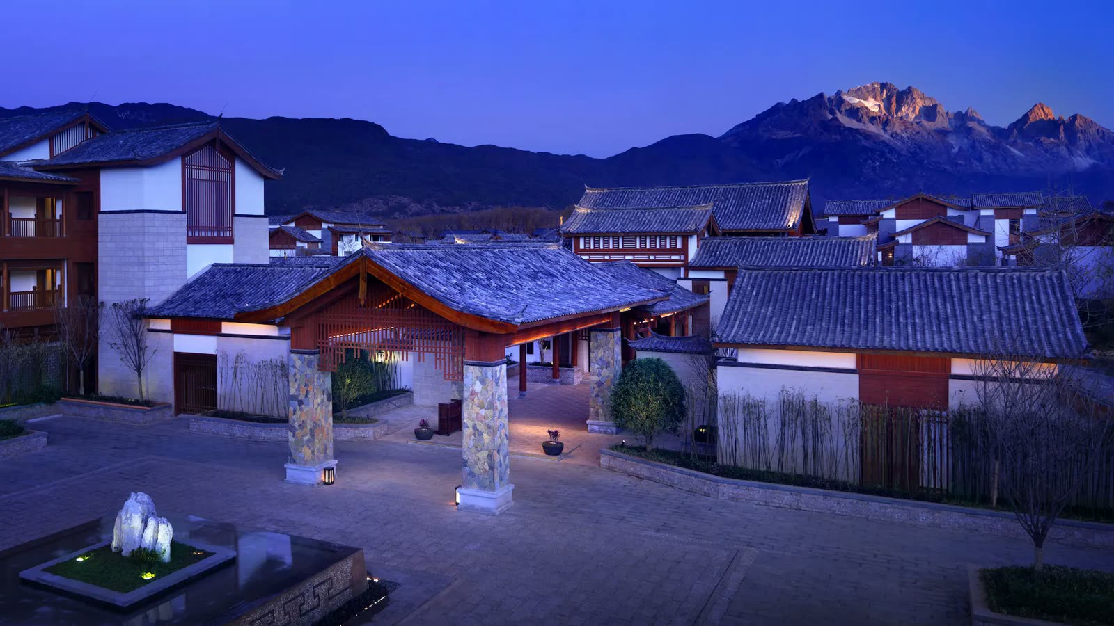 Timber entrance pavilion at Jinmao Hotel Lijiang at dusk with Jade Dragon Snow Mountain behind